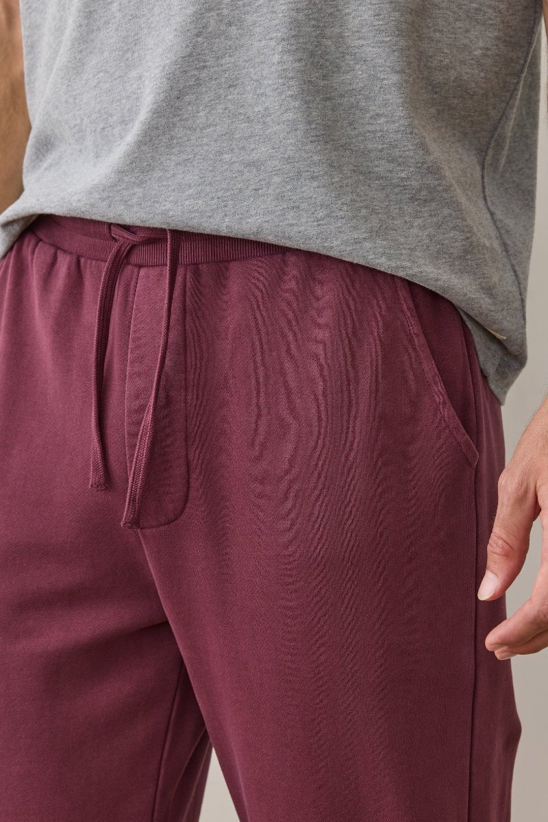 Person wearing maroon pants and a gray sleeveless shirt on a neutral background