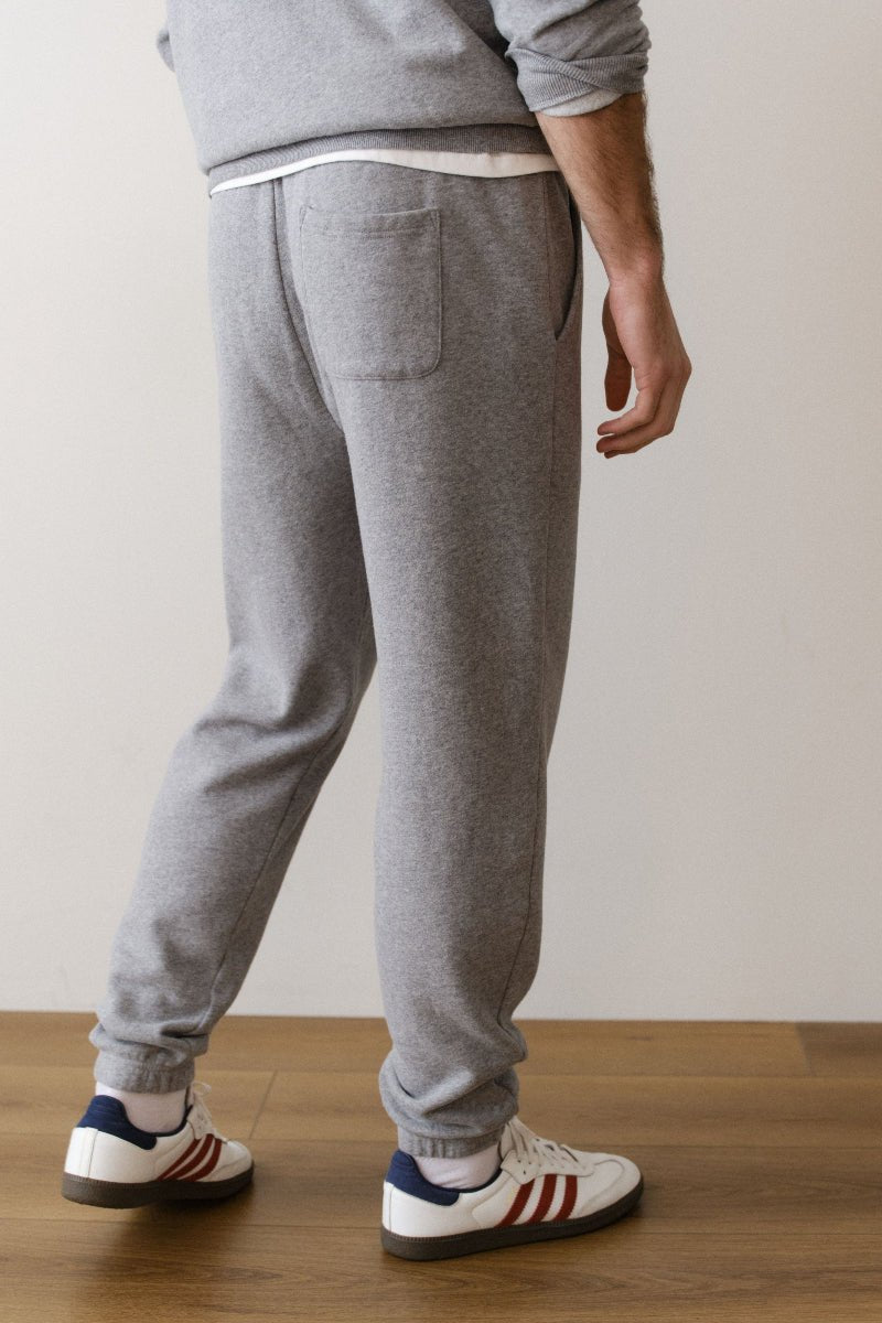 Person wearing gray sweatpants and Adidas shoes on a wooden floor with a white wall background