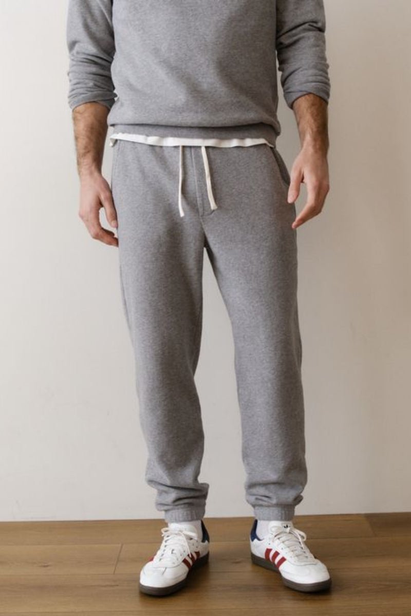 Person wearing gray sweatpants and white sneakers on a wooden floor with a beige wall background