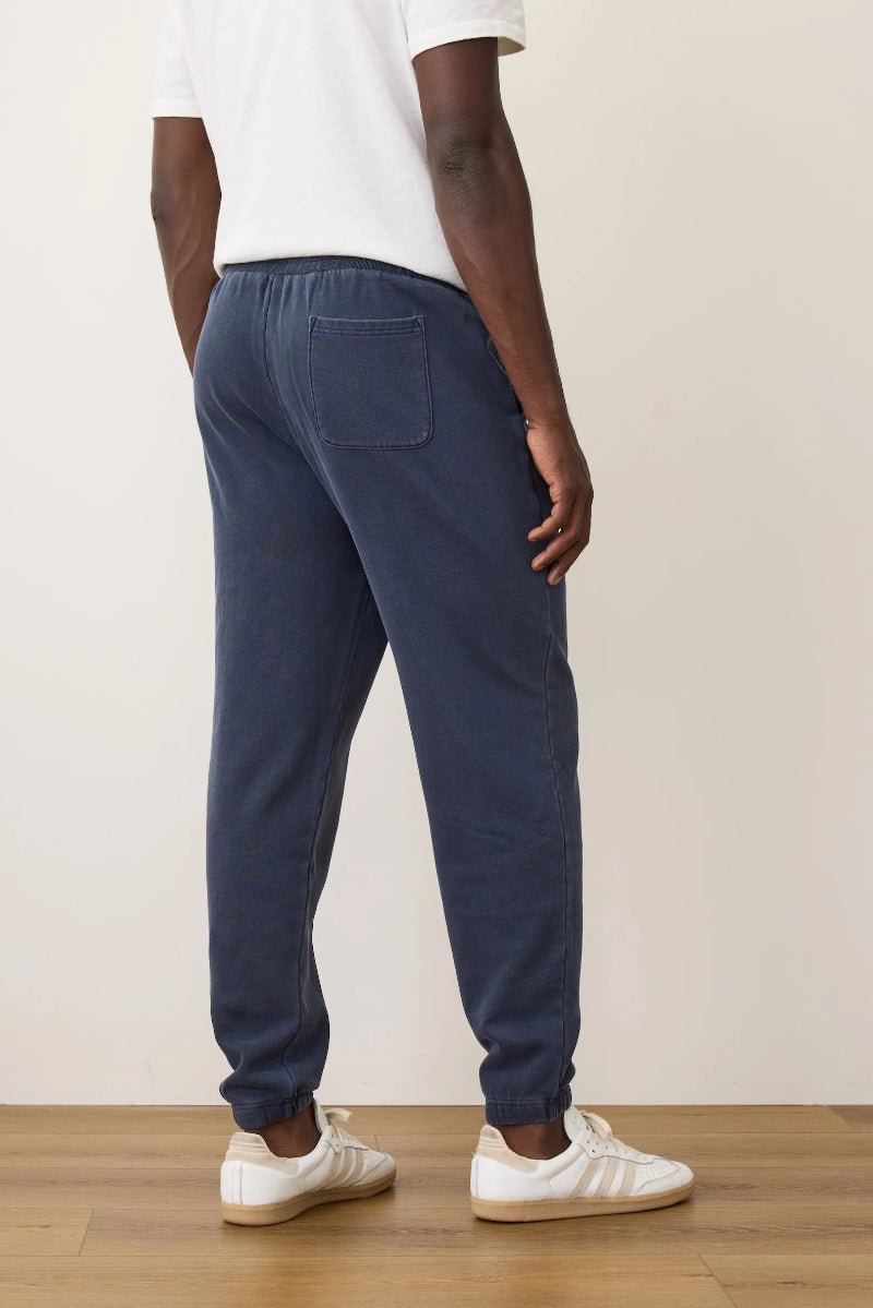 Person wearing navy sweatpants and white sneakers on a wooden floor with a beige wall background