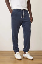 Person wearing navy jogger pants and white sneakers on a wooden floor with a beige wall background