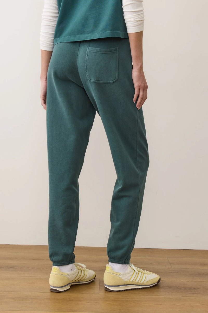 Person wearing teal pants and yellow shoes on a wooden floor with a white wall background