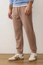 Person wearing beige sweatpants and white sneakers with black stripes on a wooden floor.