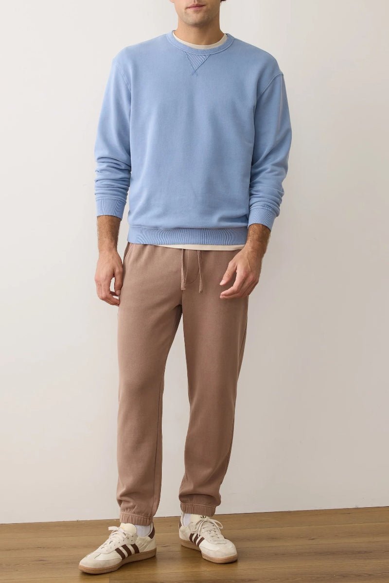 Person wearing a light blue sweater and brown pants standing against a plain white wall.