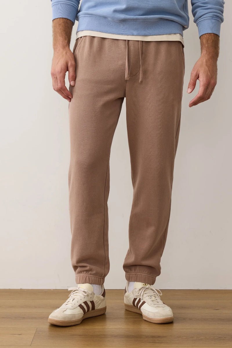 Person wearing brown sweatpants and white sneakers on a plain background