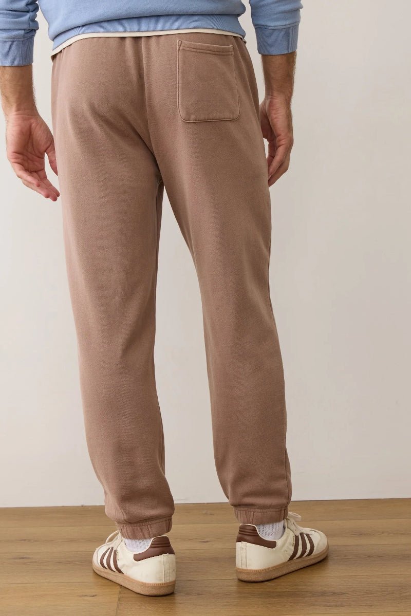 Person wearing brown sweatpants and Adidas shoes on a wooden floor.