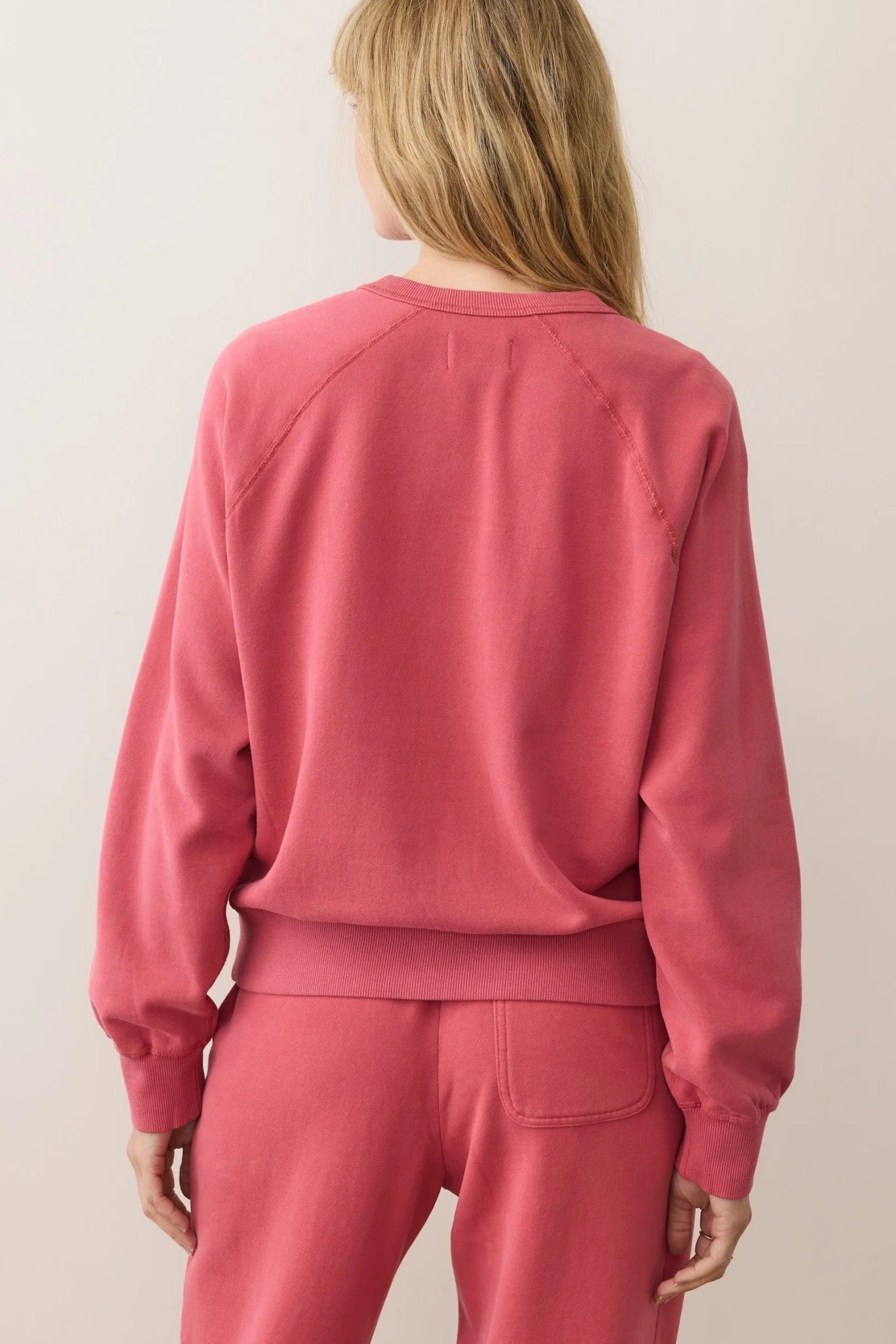 Person wearing a pink sweatshirt and pants set on a plain background