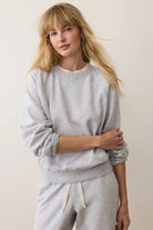 Woman wearing a gray sweatshirt and pants against a plain background