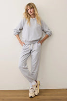 Person wearing a gray sweatshirt and pants with white sneakers against a plain wall.