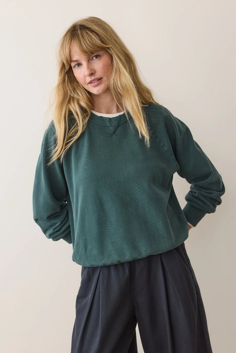 Woman wearing a green sweater and dark pants against a plain background