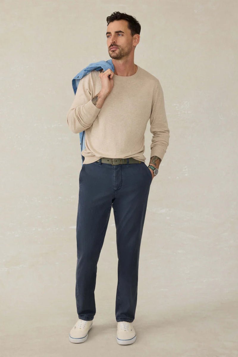 Man wearing a beige sweater and blue pants against a plain background
