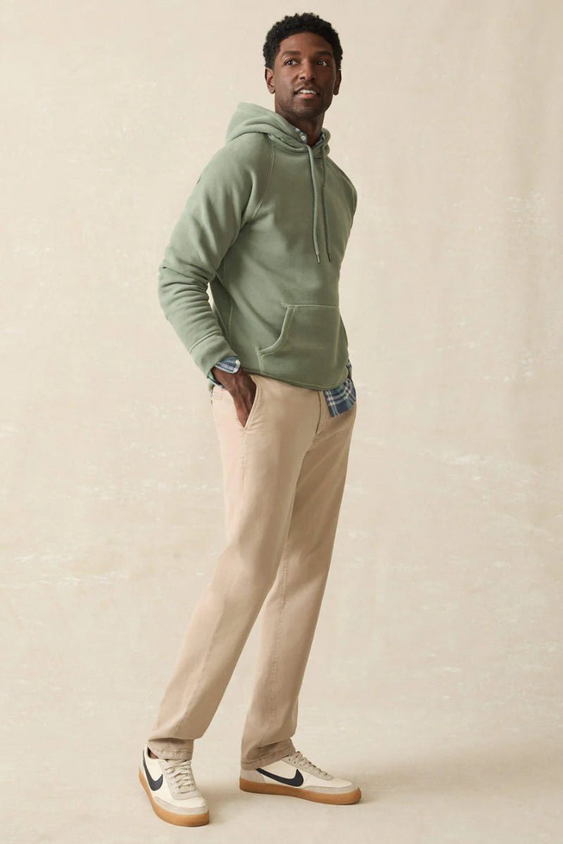 Man wearing a green hoodie and beige pants against a plain background