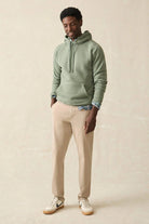 Man wearing a green hoodie and beige pants against a beige background