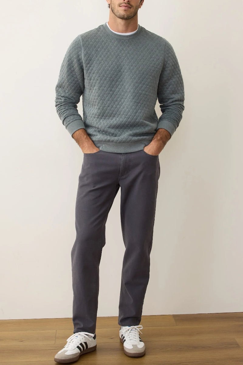 Man wearing a gray sweater and pants with white sneakers against a plain background