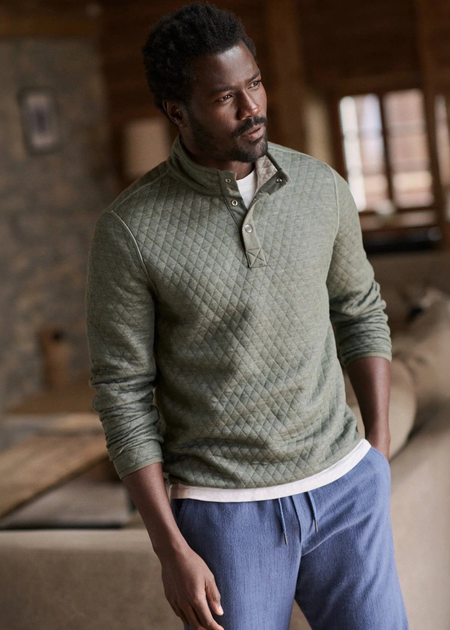 Man wearing a green quilted sweater and blue pants in a cozy indoor setting
