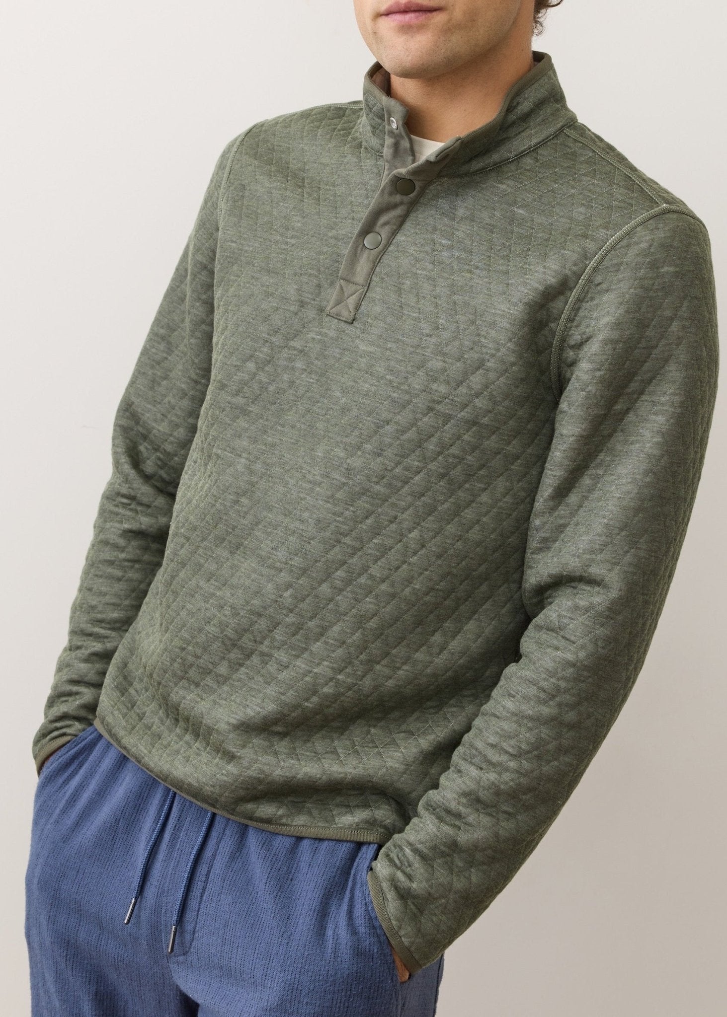 Person wearing a green quilted pullover with a neutral background