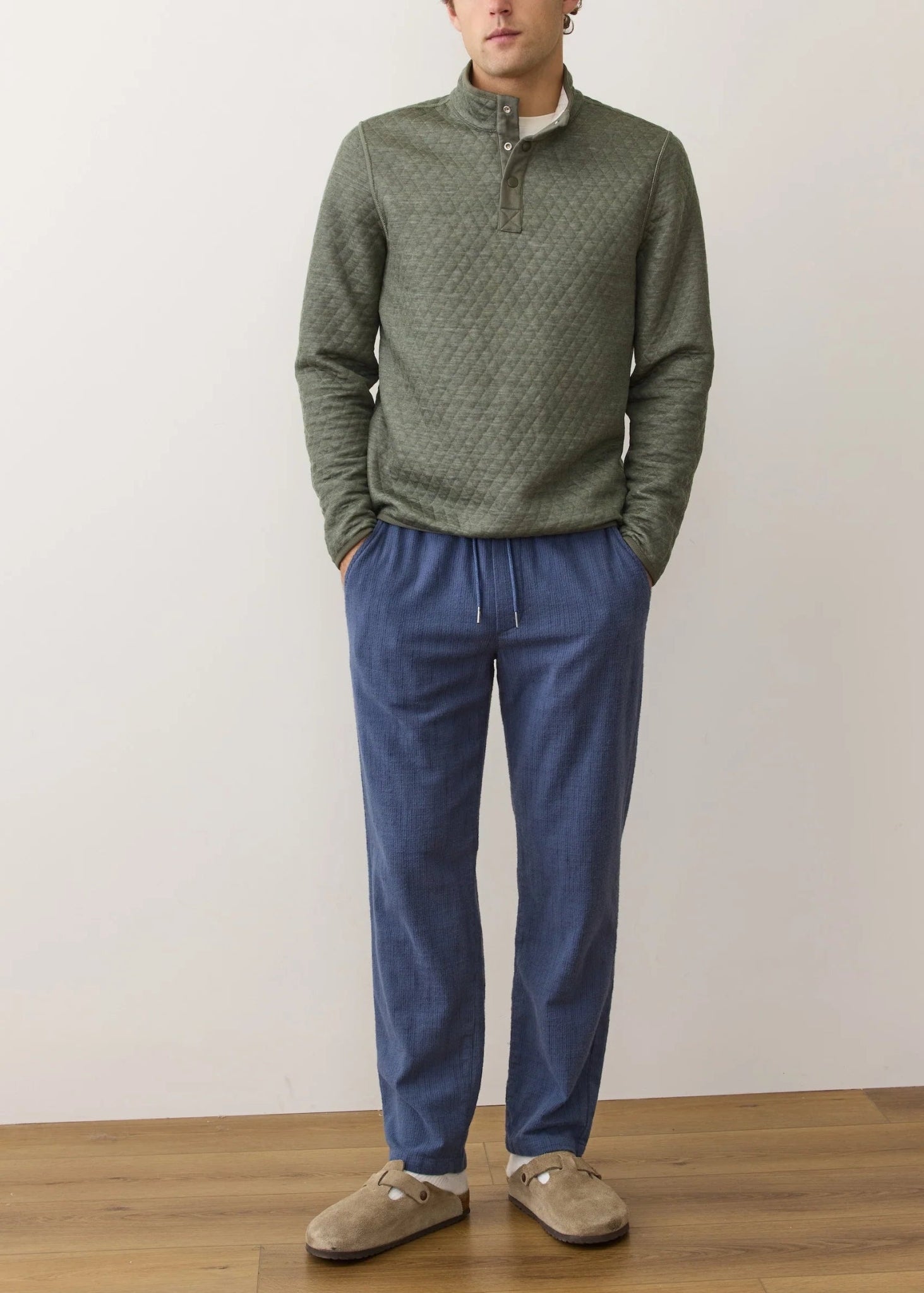 Man wearing a green patterned sweater and blue pants against a plain background