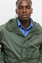 Man wearing a green jacket over a blue shirt against a plain background
