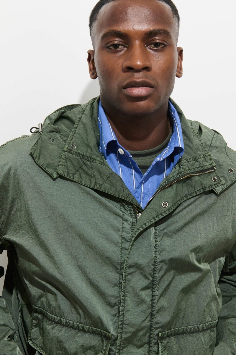 Man wearing a green jacket over a blue shirt against a plain background