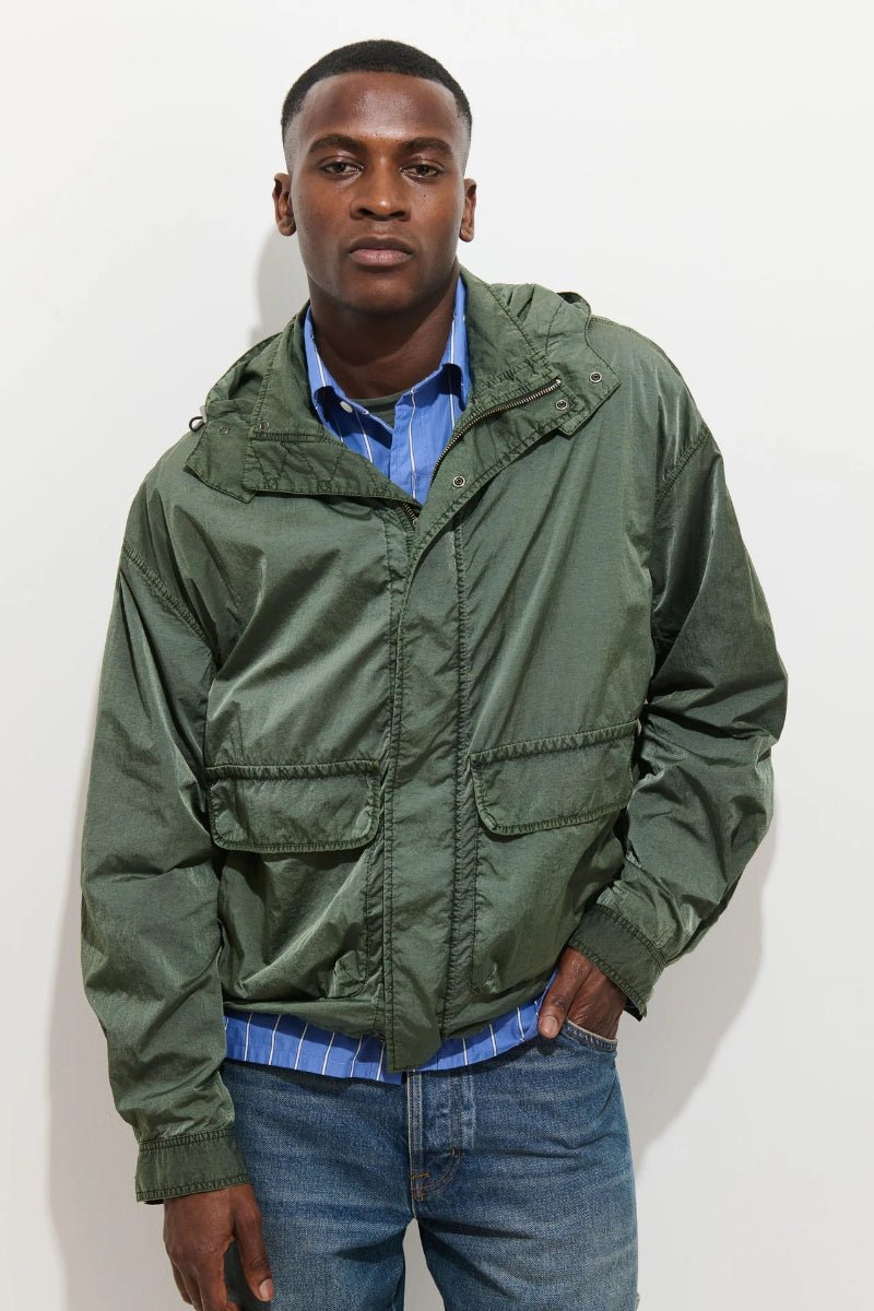 Man wearing a green jacket over a blue shirt and jeans on a white background