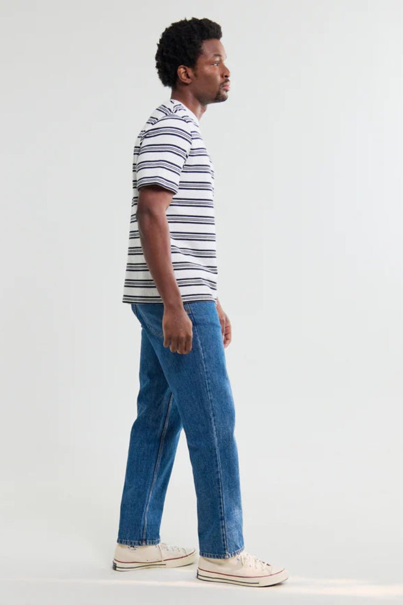 Man wearing a striped shirt and blue jeans standing against a white background