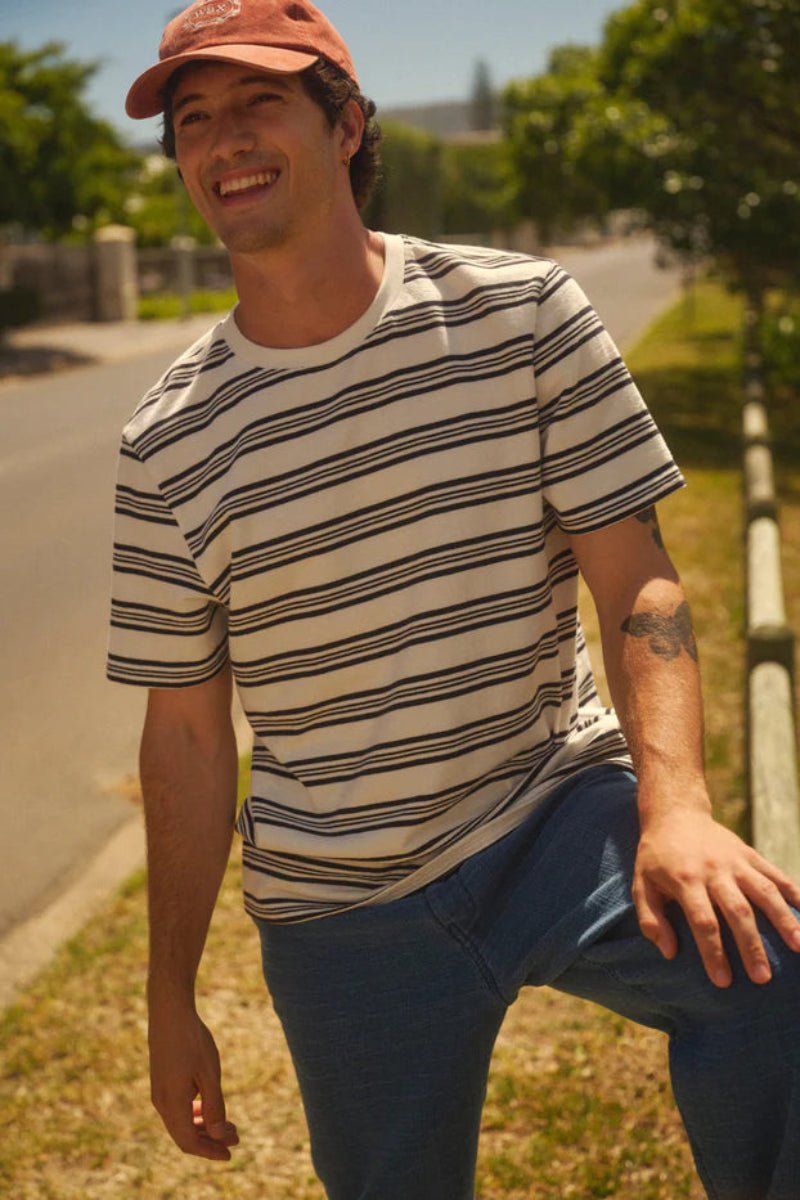 Man wearing a striped shirt and cap standing outdoors on a sunny day.
