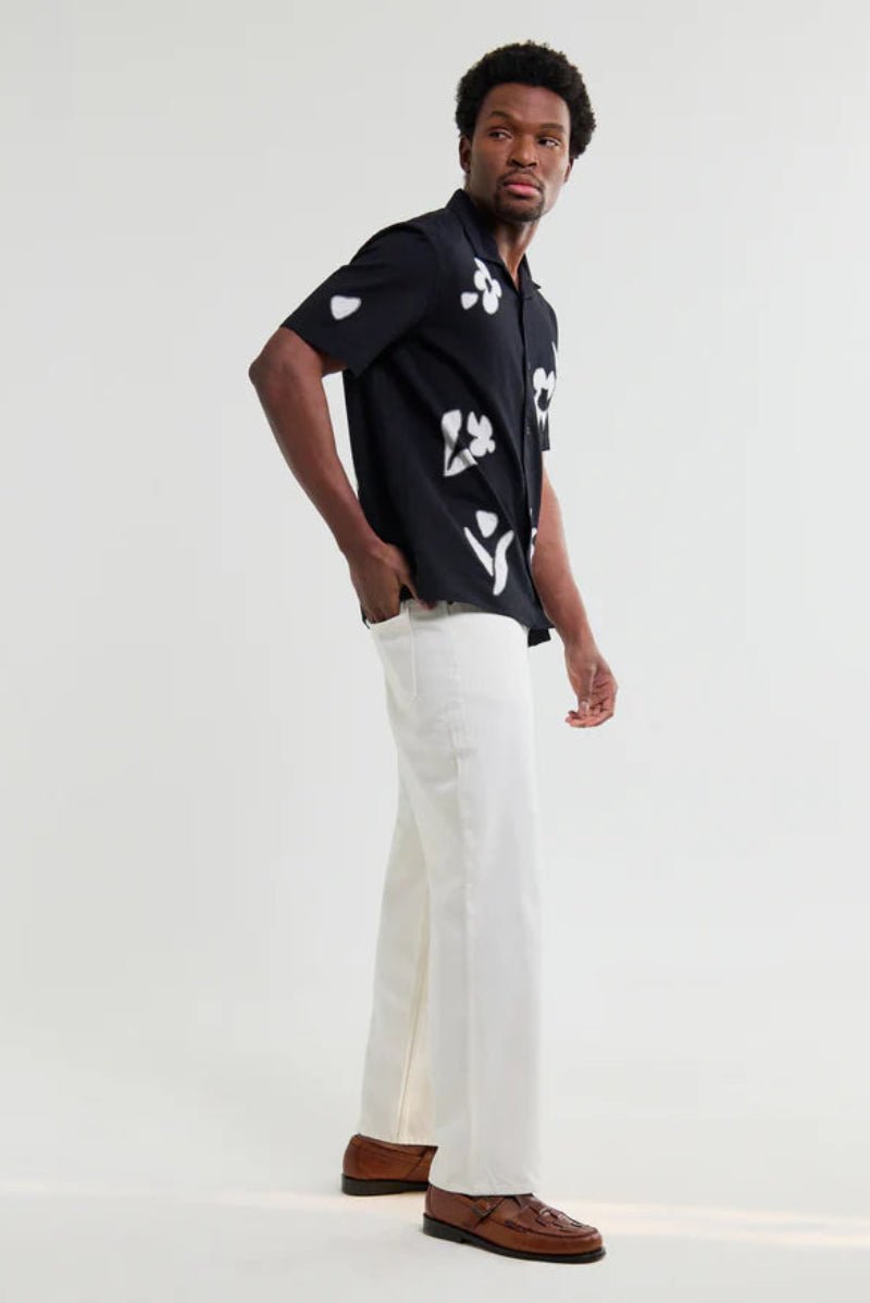 Man wearing a black patterned shirt with white pants on a white background