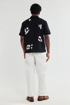 Person wearing a black shirt with white floral patterns and white pants on a white background