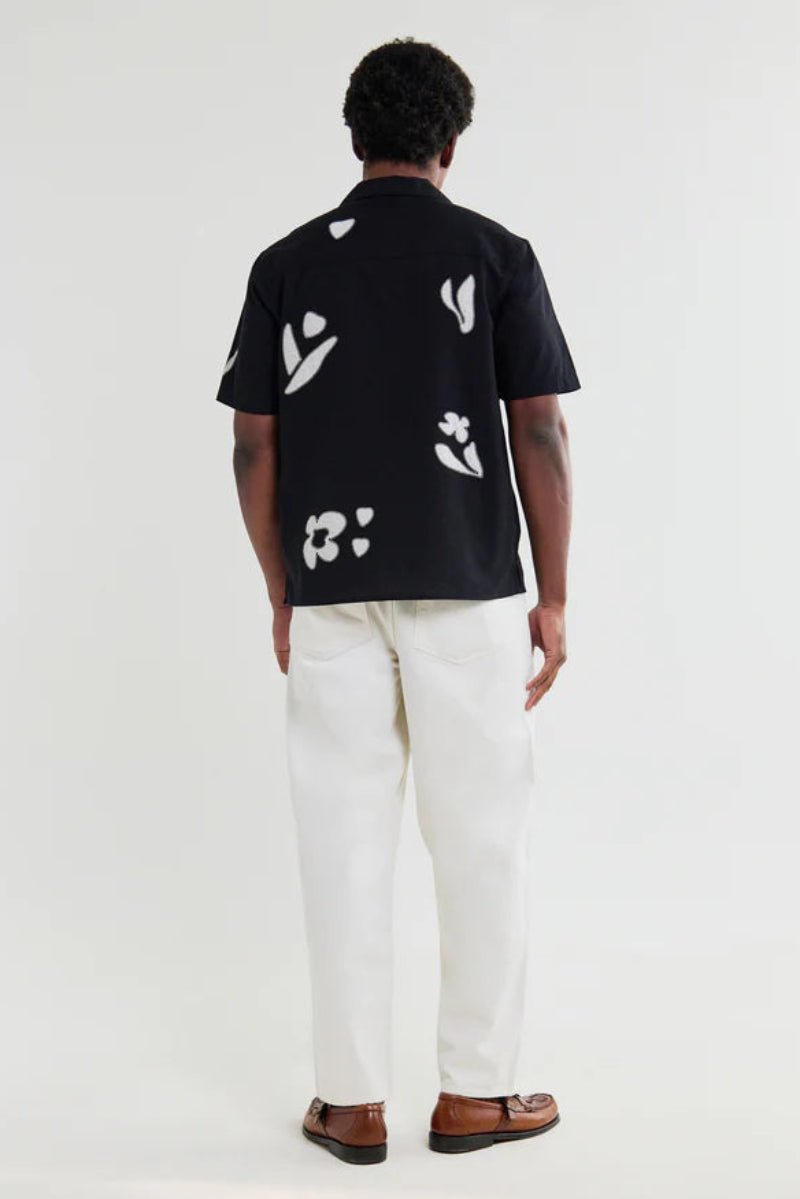 Person wearing a black shirt with white floral patterns and white pants on a white background
