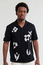 Man wearing a black shirt with white floral patterns against a plain background