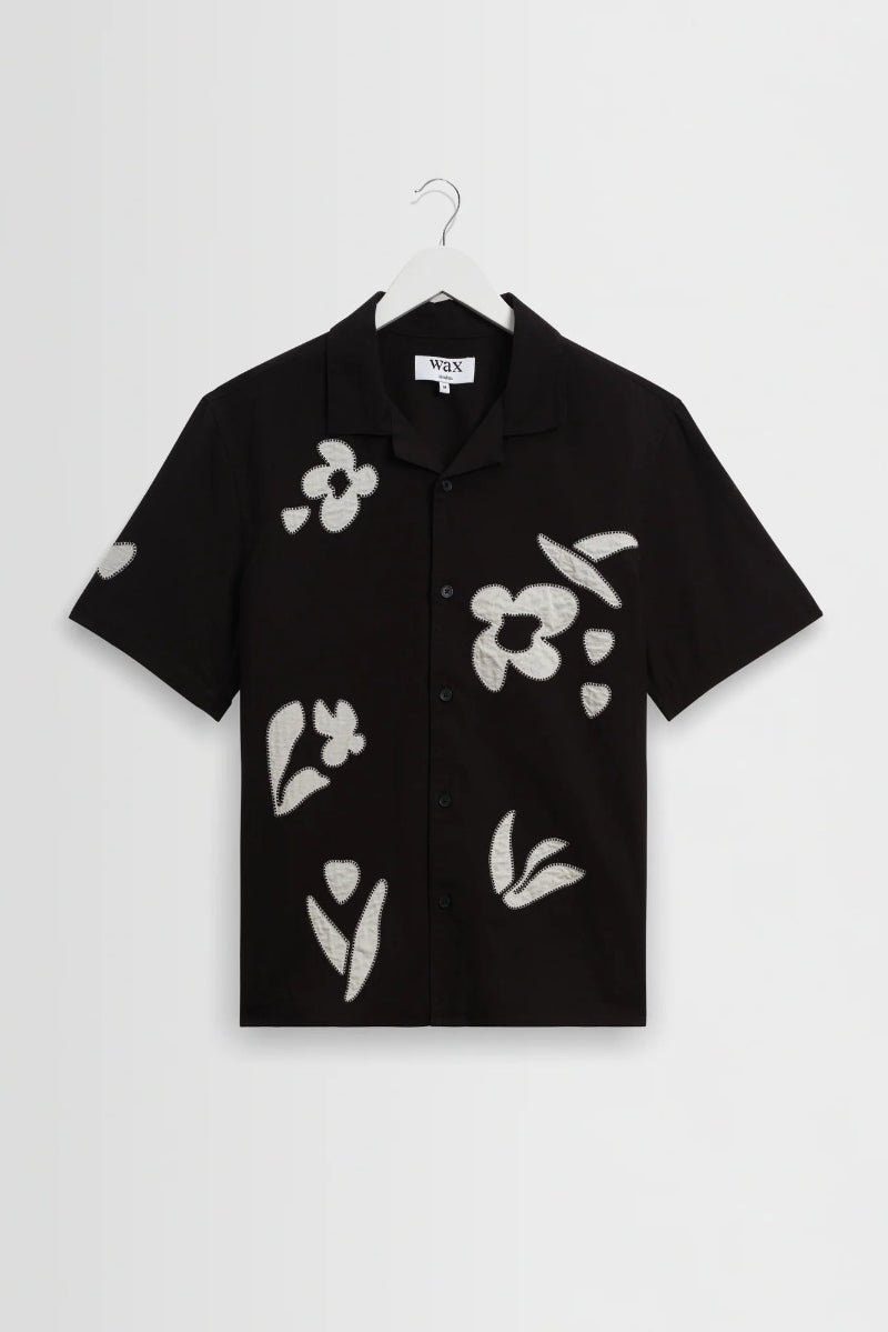 Black shirt with white floral patterns on a hanger against a light gray background