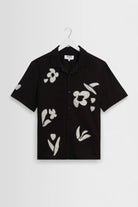 Black shirt with white floral patterns on a hanger against a light gray background