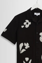 Black shirt with white floral patterns on a hanger against a white background