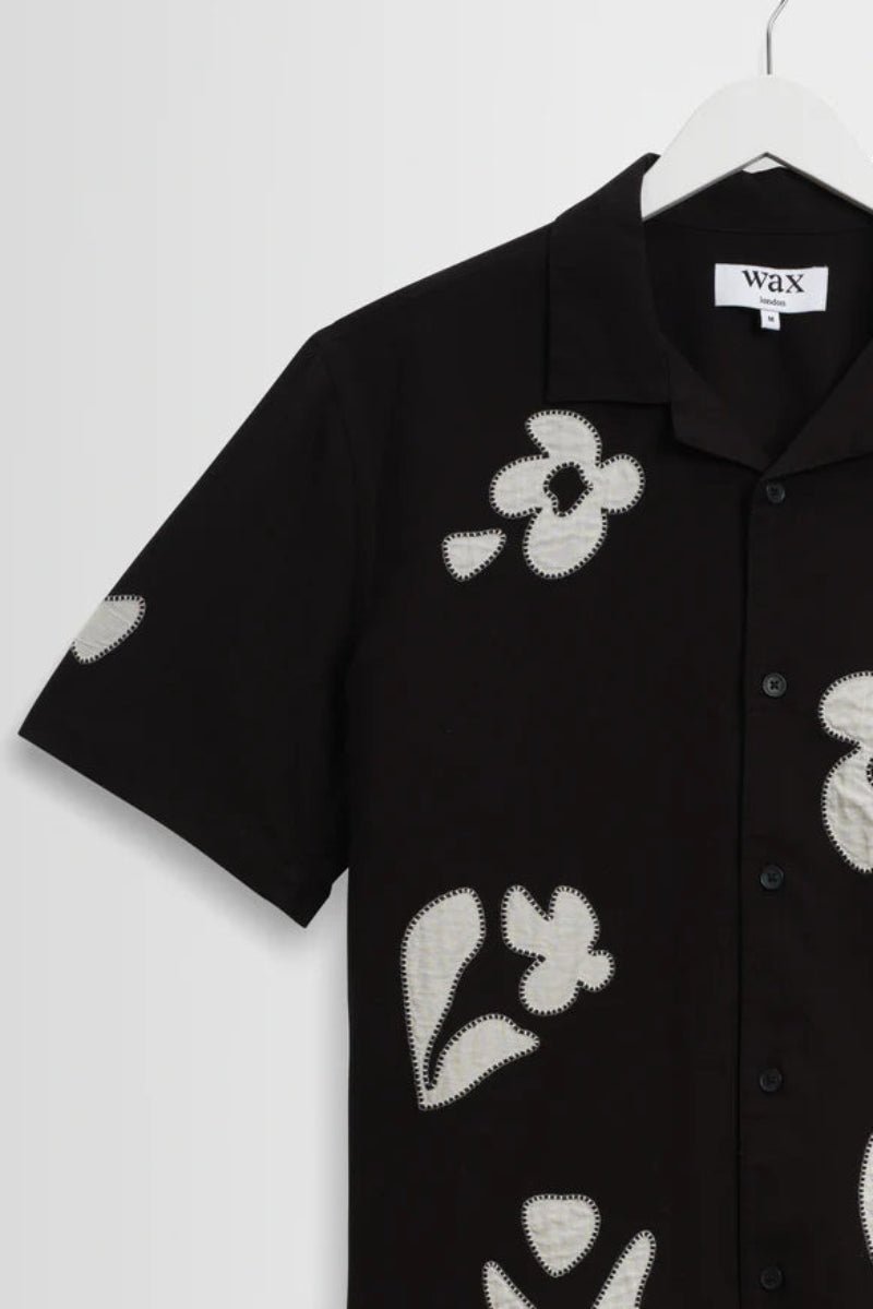 Black shirt with white floral patterns on a hanger against a white background