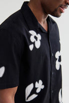 Black shirt with white floral patterns worn by a person on a plain background