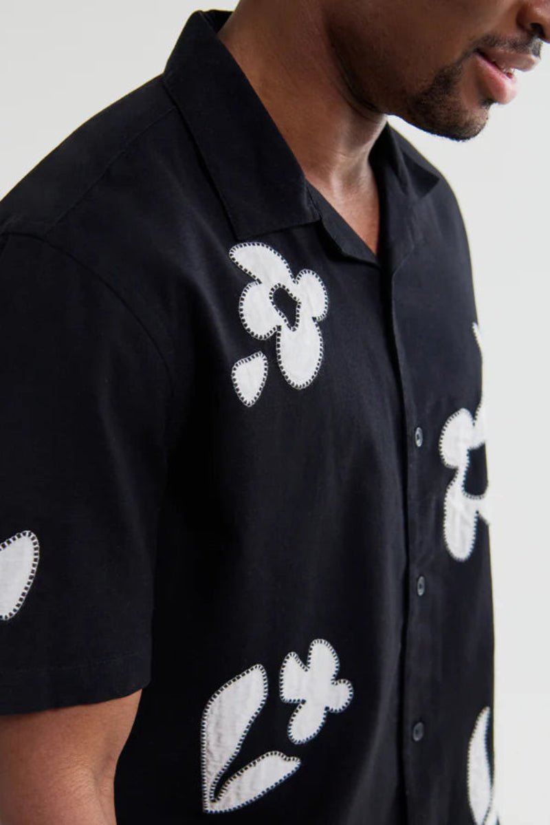 Black shirt with white floral patterns worn by a person on a plain background
