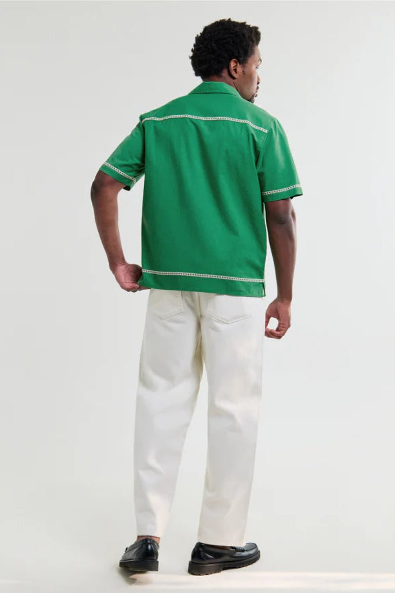 Person wearing a green shirt with white trim and white pants on a white background