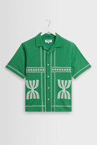 Green shirt with white patterns on a hanger against a light gray background