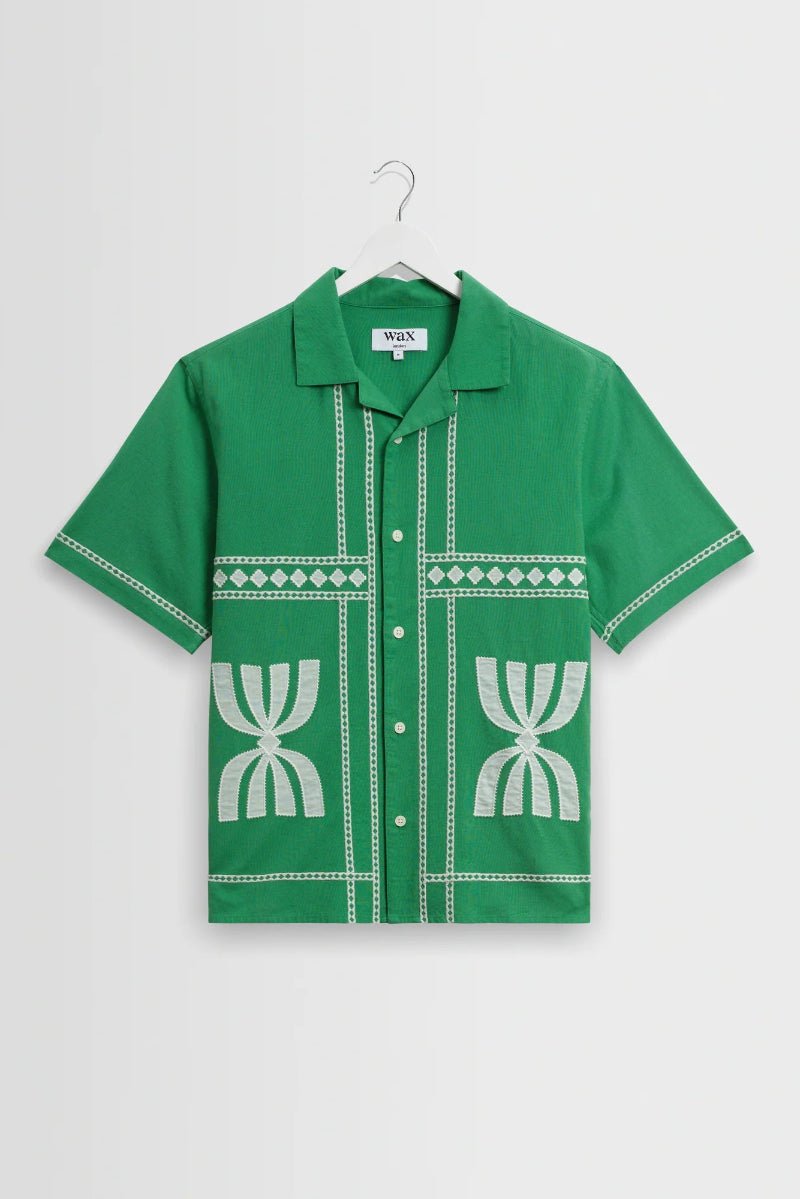 Green shirt with white patterns on a hanger against a light gray background