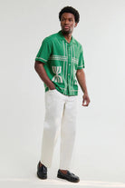 Man wearing a green patterned shirt and white pants on a white background