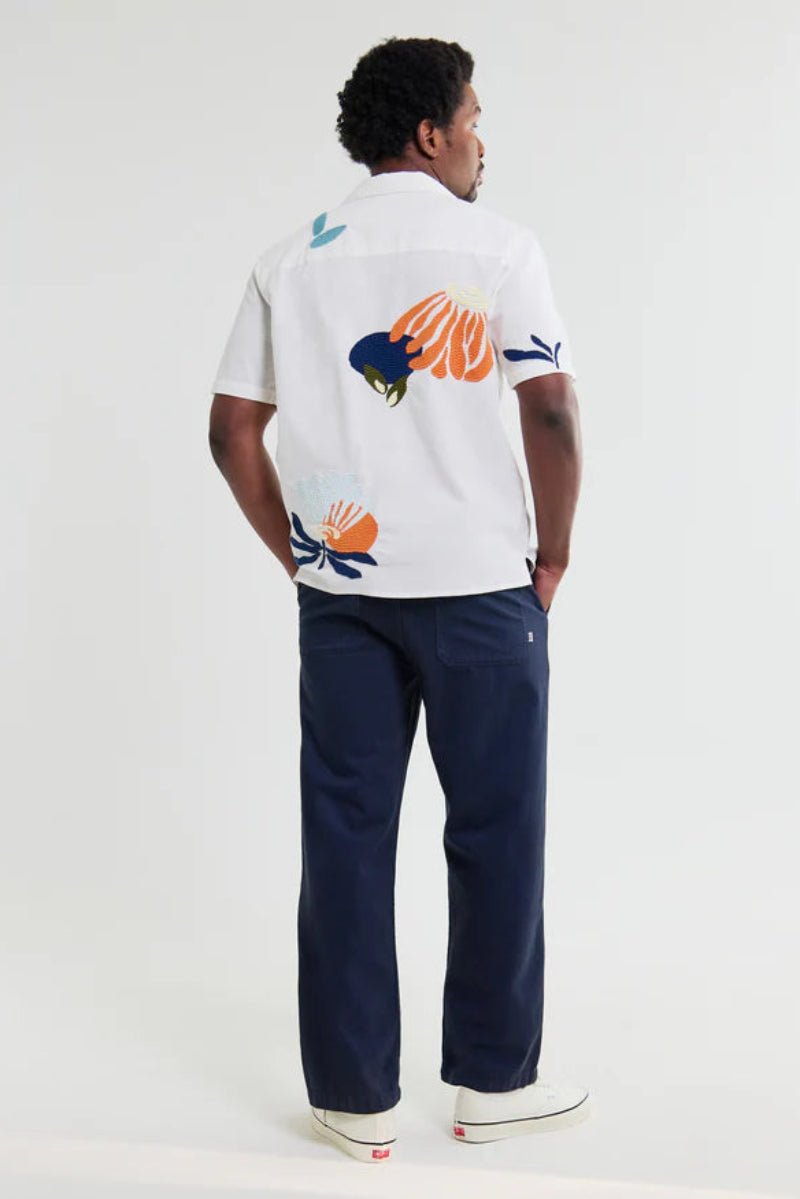 Person wearing a white shirt with colorful designs and navy pants on a white background
