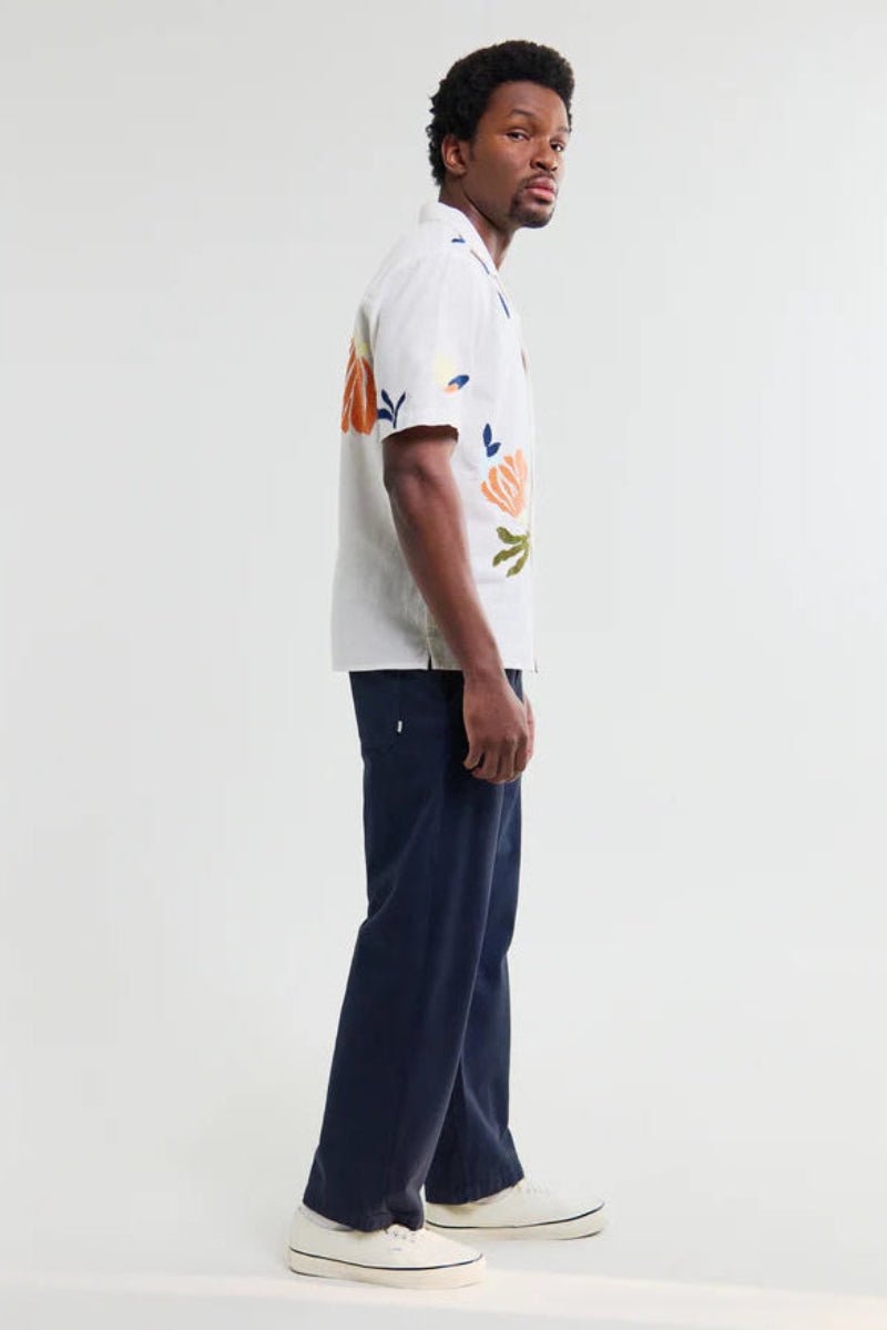 Man wearing a white floral shirt and dark pants on a white background