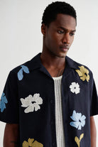 Man wearing a black shirt with floral patterns on a plain background