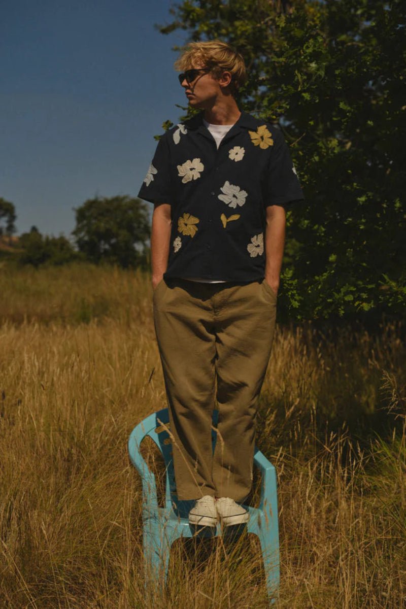 Person standing on a blue chair in a grassy field with trees in the background