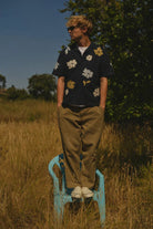 Person standing on a blue chair in a grassy field with trees in the background