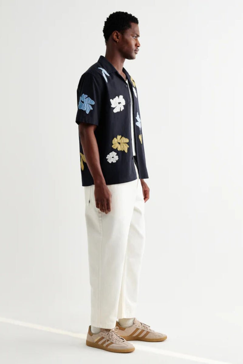 Man wearing a black floral shirt with white pants on a white background