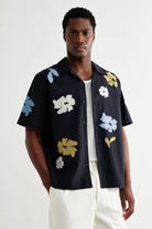 Man wearing a black short-sleeve shirt with colorful floral patterns on a white background