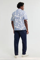 Person wearing a blue geometric patterned shirt and navy pants on a white background