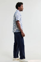 Man wearing a patterned shirt and dark pants on a white background