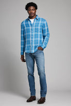 Man wearing a blue plaid shirt and jeans against a gray background